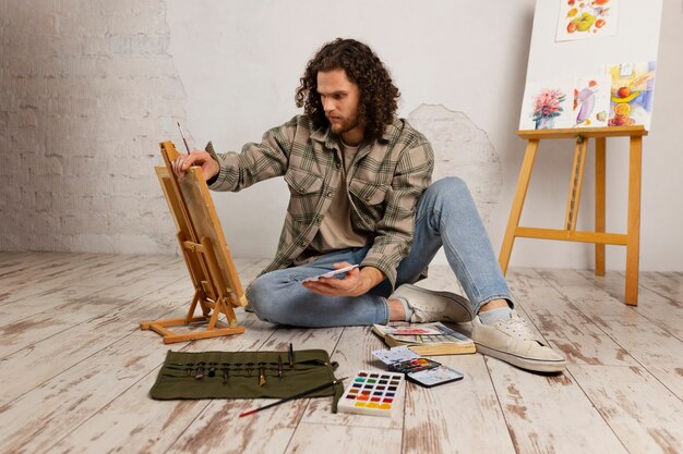 Artista masculino pintando en estudio con acuarelas.