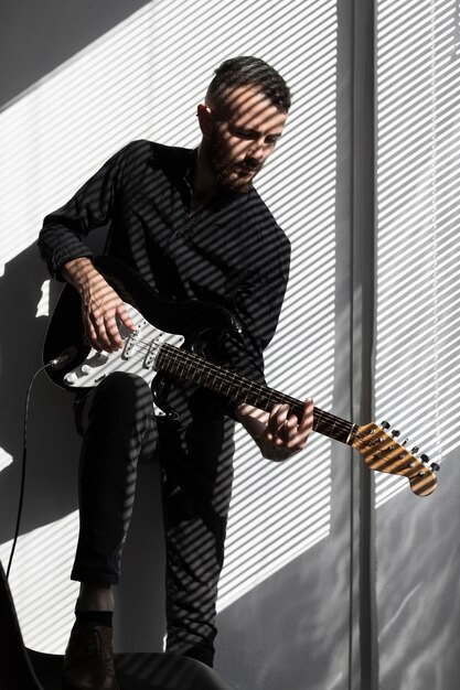 Artista masculino tocando la guitarra eléctrica con sombras de persianas