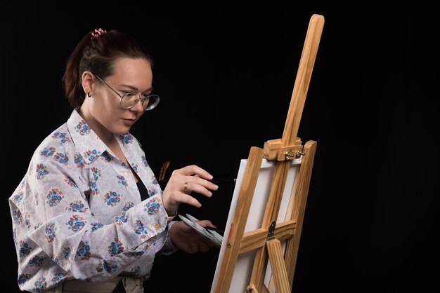 Artista mujer pinta un cuadro sobre lienzo con lápiz sobre negro
