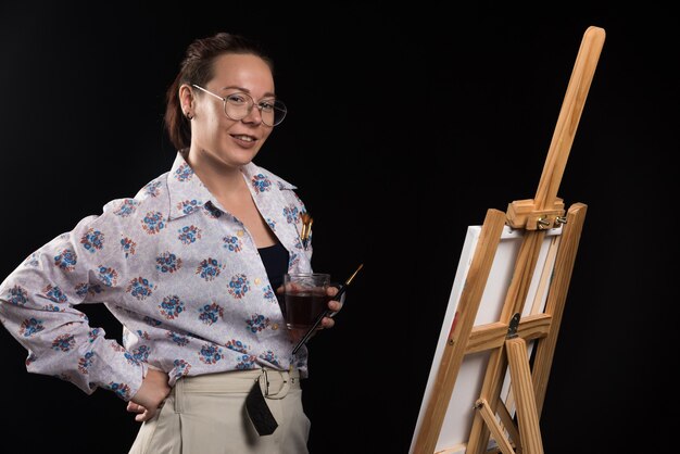 Artista mujer sosteniendo pincel y lienzo sobre fondo negro. Foto de alta calidad