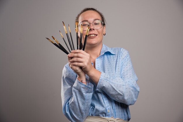 Artista mujer sostiene pinceles sobre fondo gris. Foto de alta calidad