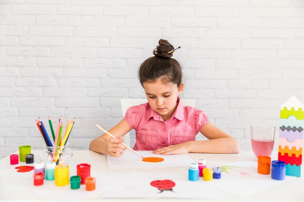 Artista niño pintando sobre papel blanco sobre el escritorio contra la pared de ladrillo blanco