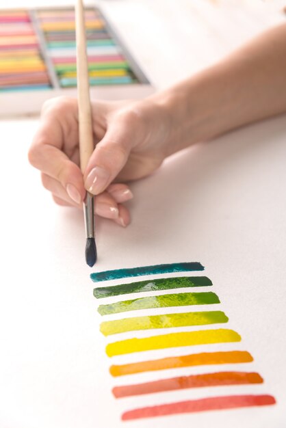 Artista pintando rayas de colores con pincel sobre papel blanco