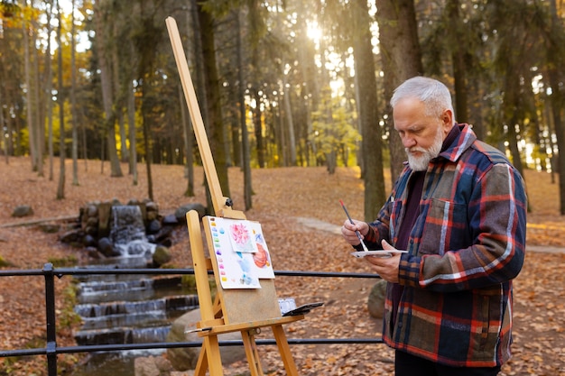 Foto gratuita artista de pintura de acuarela al aire libre en el bosque con caballete y lienzo