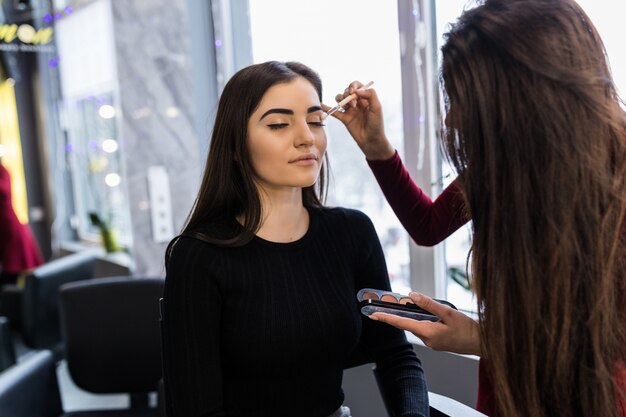 Artista profesional pone maquillaje en polvo en modelo con suéter negro
