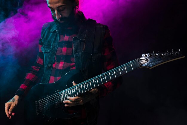 Artista tocando la guitarra y la luz del escenario violeta y humo.