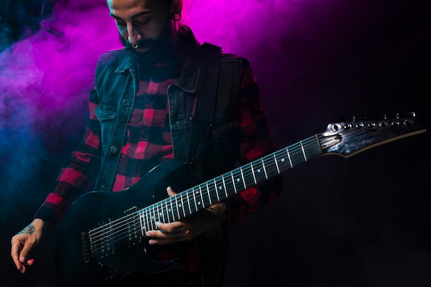 Artista tocando la guitarra y la luz del escenario violeta y humo.