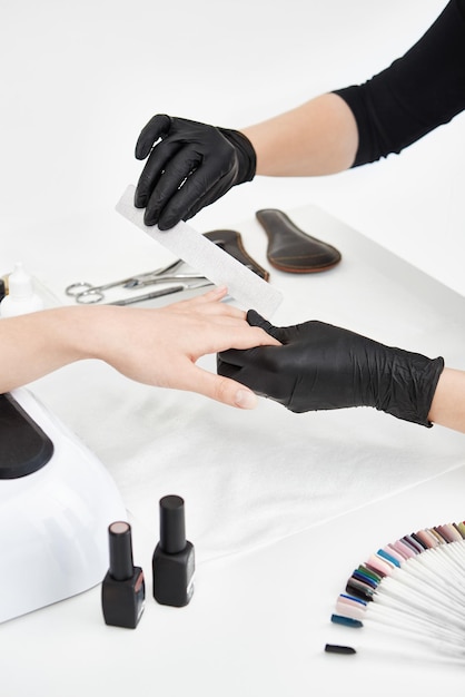 Artista de uñas profesional que trabaja con lima de uñas haciendo uñas cuadradas mientras hace manicura en el salón.