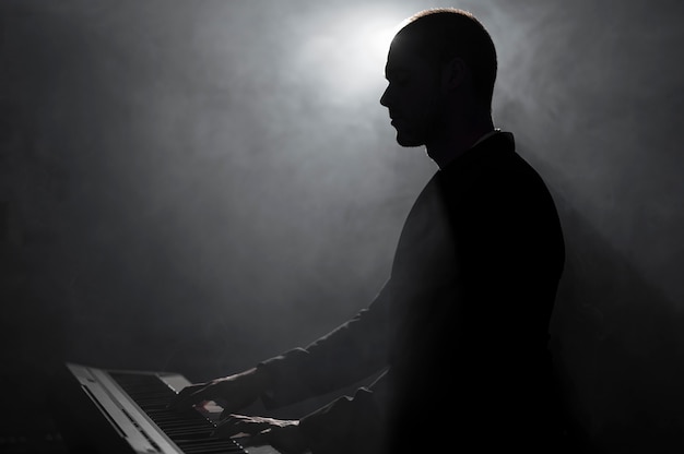 Artista de vista lateral tocando el piano efectos de humo y sombras