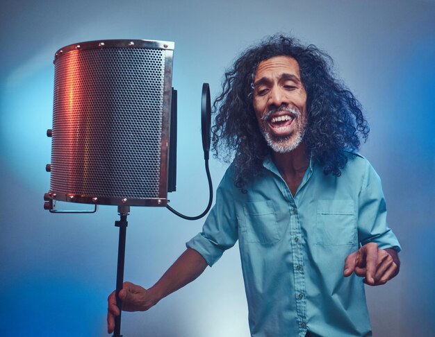 Artista vocal africano con una camisa azul escribiendo emocionalmente una canción en el estudio de grabación. Aislado sobre un fondo azul.