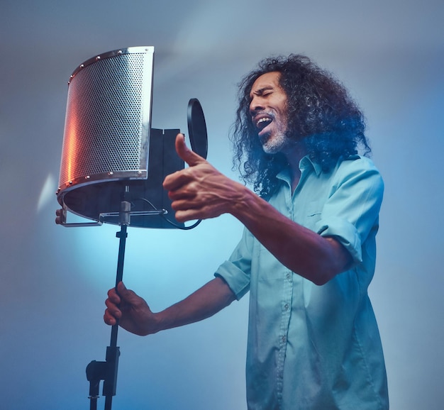 Foto gratuita artista vocal africano con una camisa azul escribiendo emocionalmente una canción en el estudio de grabación. aislado sobre un fondo azul.