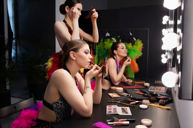 Artistas femeninas de cabaret preparándose entre bastidores con maquillaje