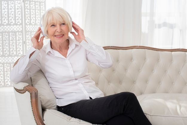 Aseado anciana sentada en el sofá con auriculares