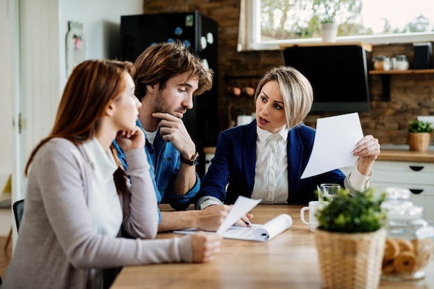 Foto gratuita asesor financiero comunicándose con una pareja joven mientras revisa sus informes financieros durante una reunión en casa