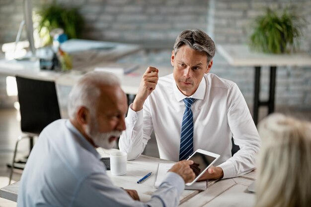 Asesor financiero y pareja de ancianos que usan una tableta digital mientras tienen una reunión en la oficina