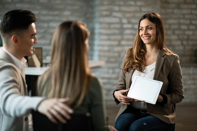 Asesor financiero sonriente reuniéndose con una pareja joven y mostrándoles posibilidades de inversión en el panel táctil de la oficina