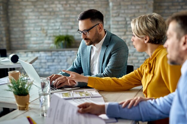 Asesor financiero trabajando en una computadora mientras se reúne con una pareja en la oficina