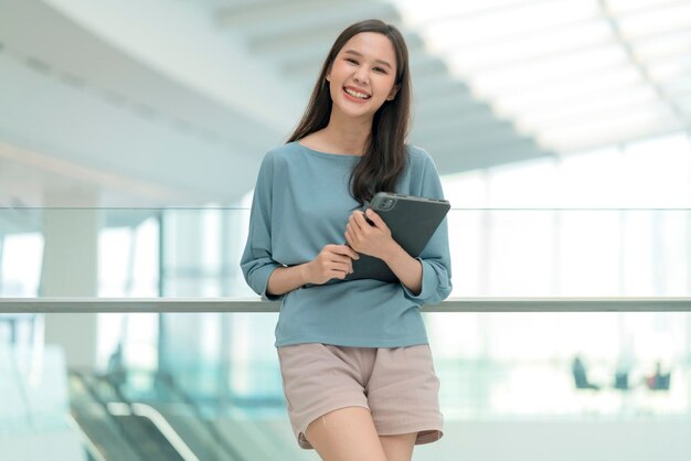 Asia sonriente alegre mujer nómada digital dispositivo de mano sujetar tableta mirar cámara retrato shothappiness sonriente asia mujer de pie en el pasillo de la universidad de oficina con actitud sonriente positiva