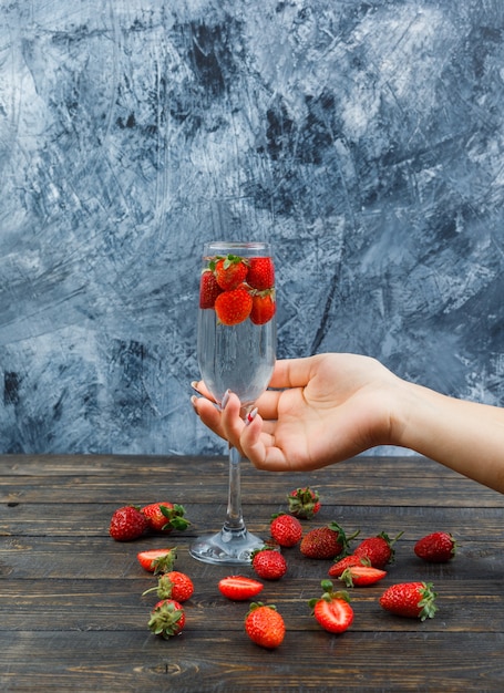 Asimiento de la mano copa de vino y fresas en una copa de vino sobre una superficie de piedra oscura. vista lateral.