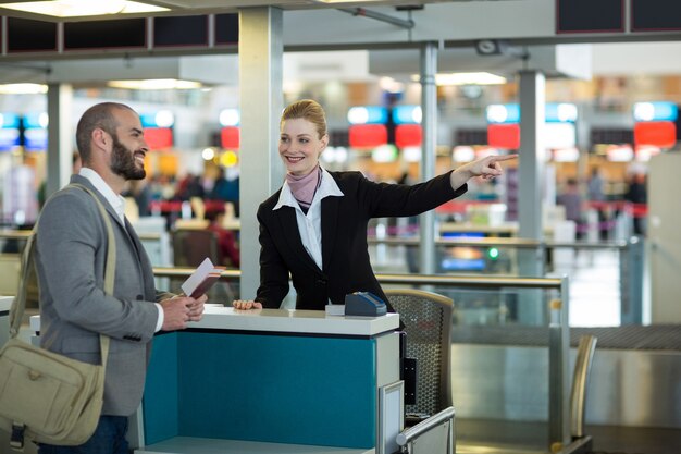 Asistente de check-in de la aerolínea que muestra la dirección al viajero en el mostrador de check-in