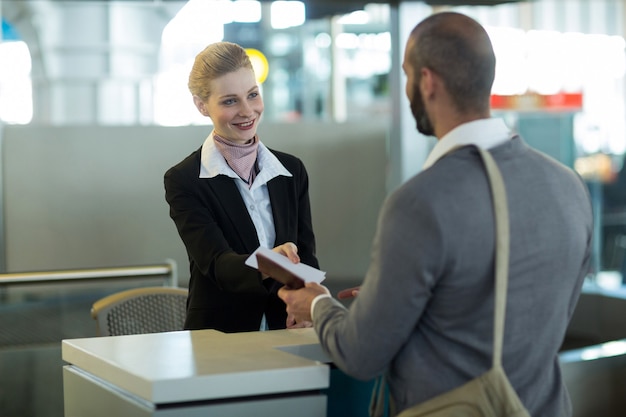 Asistente de facturación de la aerolínea que entrega el pasaporte al viajero