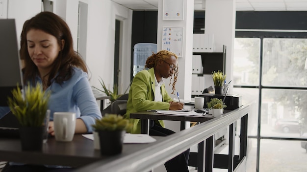 Asistente femenina escribiendo datos en documentos, tomando notas en papeles para crear un informe anual. Inversión de planificación de empleados ejecutivos con análisis y estadísticas en portátiles y archivos.