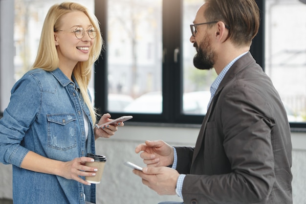 Foto gratuita asistente femenina positiva y empresario masculino serio barbudo en la oficina