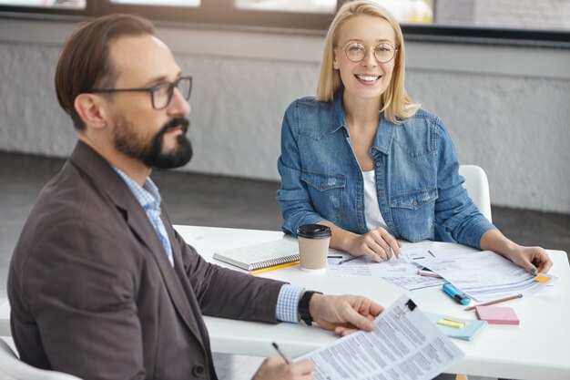 Asistente femenina positiva y empresario masculino serio barbudo en la oficina