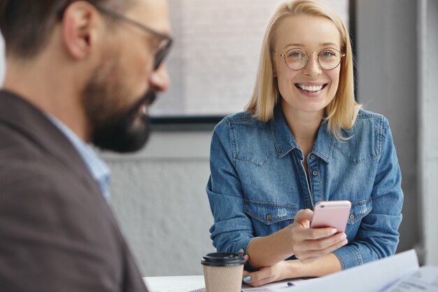 Asistente femenina positiva y empresario masculino serio barbudo en la oficina