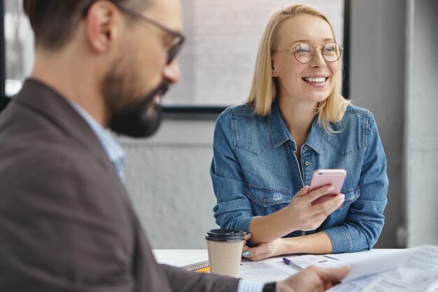 Asistente femenina positiva y empresario masculino serio barbudo en la oficina