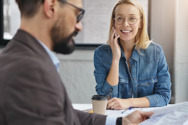 Asistente femenina positiva y empresario masculino serio barbudo en la oficina