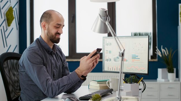 Asistente financiero que trabaja en una aplicación de teléfono inteligente con estadísticas, usando un teléfono móvil para navegar por Internet en busca de una estrategia de crecimiento empresarial. Presentación de investigación de planificación de empleados masculinos en la oficina.