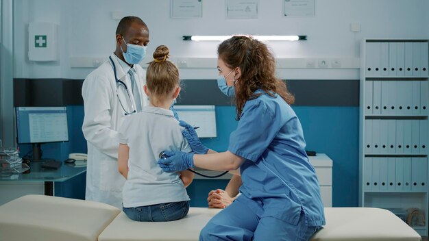 Asistente médico consultando a un niño con estetoscopio en el gabinete en la cita de control. Enfermera que usa una herramienta para medir los latidos del corazón y el pulso, brindando asistencia y apoyo al niño y a la madre