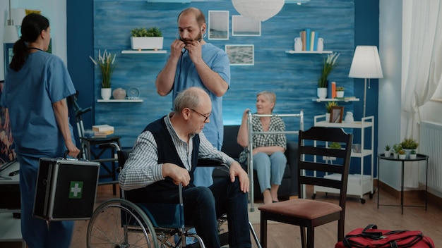 Asistente médico que consulta a un jubilado con discapacidad crónica que usa estetoscopio para medir los latidos del corazón y el pulso en un hogar de ancianos. Paciente discapacitado en silla de ruedas haciendo chequeo con enfermera