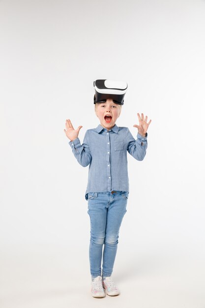 Asombrado del futuro. Niña o niño en jeans y camisa con gafas de casco de realidad virtual aisladas sobre fondo blanco de estudio. Concepto de tecnología de punta, videojuegos, innovación.