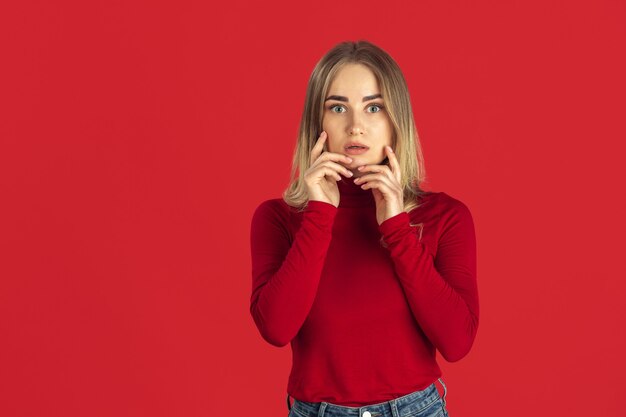 Asombrado. Retrato monocromo de joven mujer rubia caucásica aislada en pared roja. Modelo de mujer hermosa en camisa. Las emociones humanas, la expresión facial, las ventas, el concepto publicitario. Cultura juvenil.