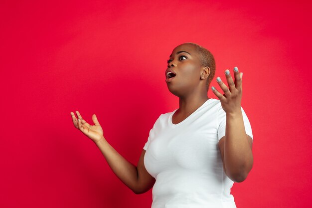 Asombrado. Retrato de mujer joven afroamericana en rojo. Hermosa modelo de mujer en camisa