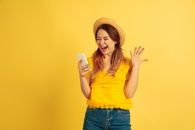 Asombrado usando un teléfono inteligente. Retrato de mujer caucásica sobre fondo amarillo de estudio.