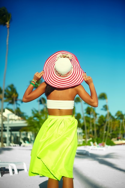 Aspecto de alta moda. Detrás de glamour modelo sexy mujer en tela colorida y sombrero para el sol detrás del cielo azul de la playa