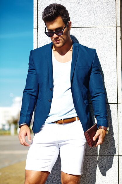 Aspecto de alta moda Joven elegante confiado feliz apuesto hombre de negocios modelo hombre en traje azul ropa en la calle con gafas de sol detrás del cielo