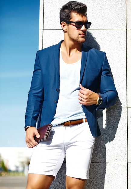 Aspecto de alta moda Joven elegante confiado feliz apuesto hombre de negocios modelo hombre en traje azul ropa en la calle con gafas de sol detrás del cielo