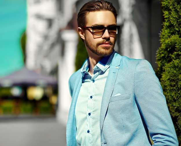 Foto gratuita aspecto de alta moda joven elegante y confiado feliz apuesto hombre de negocios modelo en traje en la calle con gafas de sol