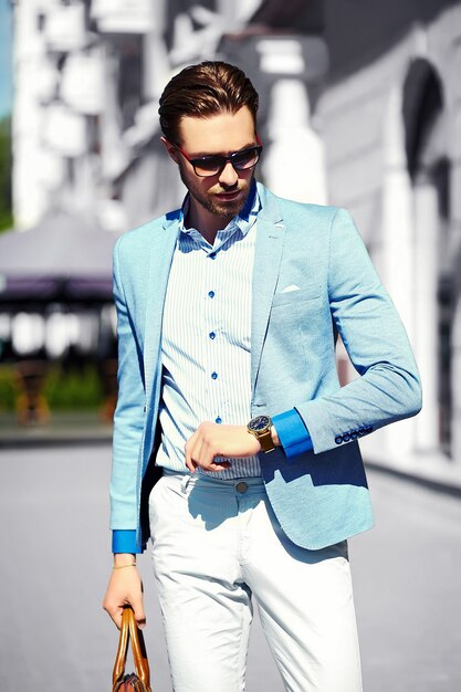 Aspecto de alta moda Joven elegante y confiado feliz apuesto hombre de negocios modelo en traje de estilo de vida en la calle en gafas de sol mira su reloj