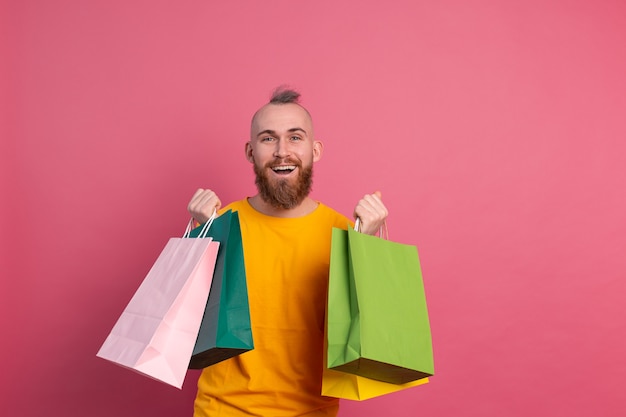 Aspecto casual del hombre positivo barbudo feliz con el fondo rosado del estudio de las bolsas de compras coloridas