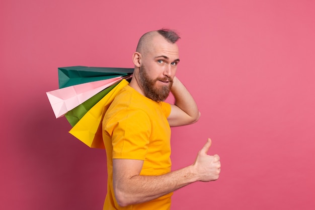 Aspecto casual del hombre positivo barbudo feliz con el fondo rosado del estudio de las bolsas de compras coloridas