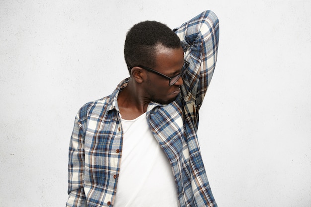 Foto gratuita asqueado macho joven con camisa a cuadros y gafas con olor a axila húmeda y sudorosa después de una reunión estresante, sintiendo náuseas y frunciendo los labios. el hombre negro no soporta el mal olor. hiperhidrosis e higie