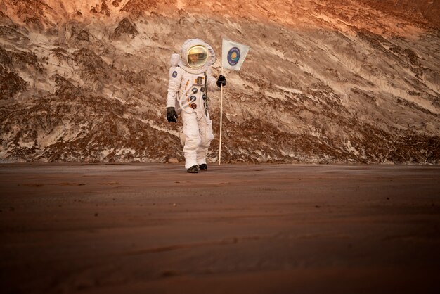 Astronauta masculino sosteniendo una bandera atascada en el suelo en un planeta desconocido