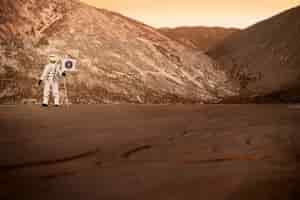 Foto gratuita astronauta masculino sosteniendo una bandera atascada en el suelo en un planeta desconocido