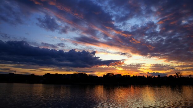 Atardecer en Moldavia, exuberantes nubes con luz amarilla reflejada en la superficie del agua en primer plano