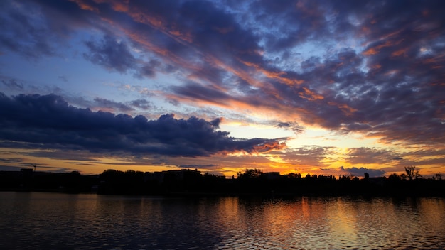 Atardecer en Moldavia, exuberantes nubes con luz amarilla reflejada en la superficie del agua en primer plano